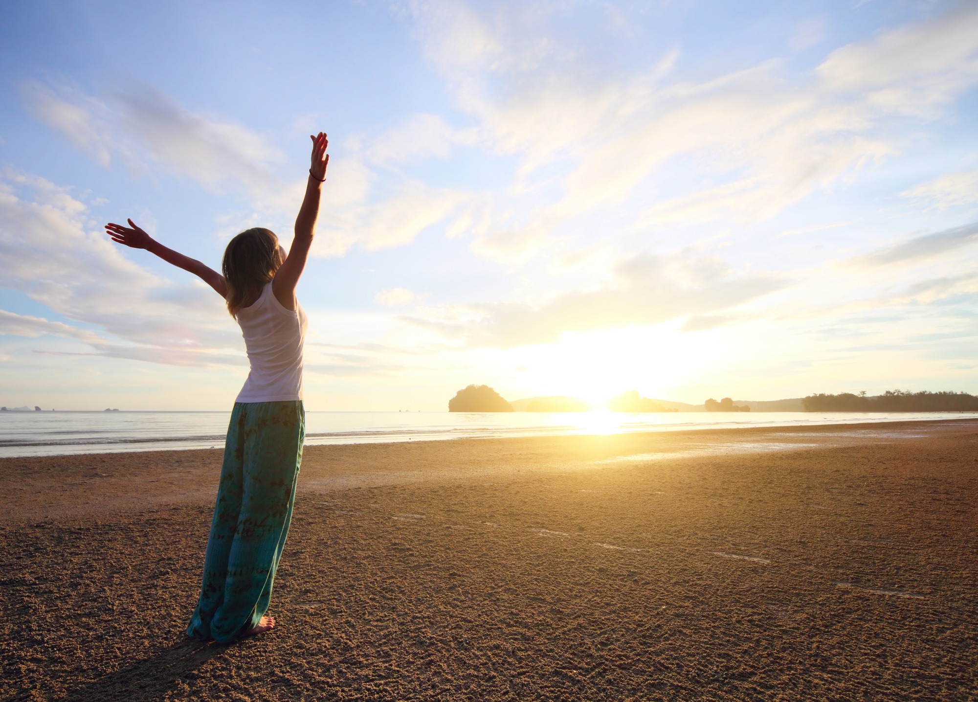 Young woman with raised hands standing on sand and looking to a sky